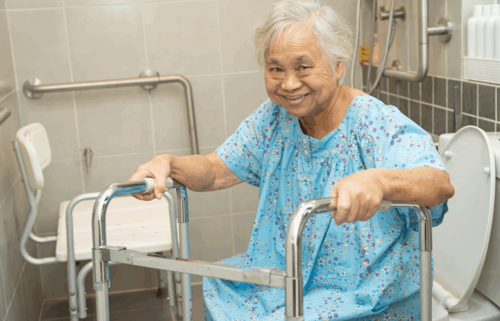 Smiling elderly woman using grab rails and a walker in an accessible bathroom with a shower chair, designed for safety in retirement villages.
