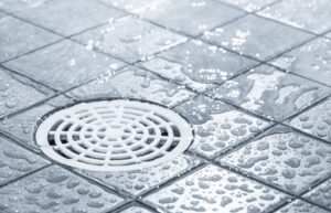 Close-up of a shower floor with water droplets on tiles, showing the drain in the center.