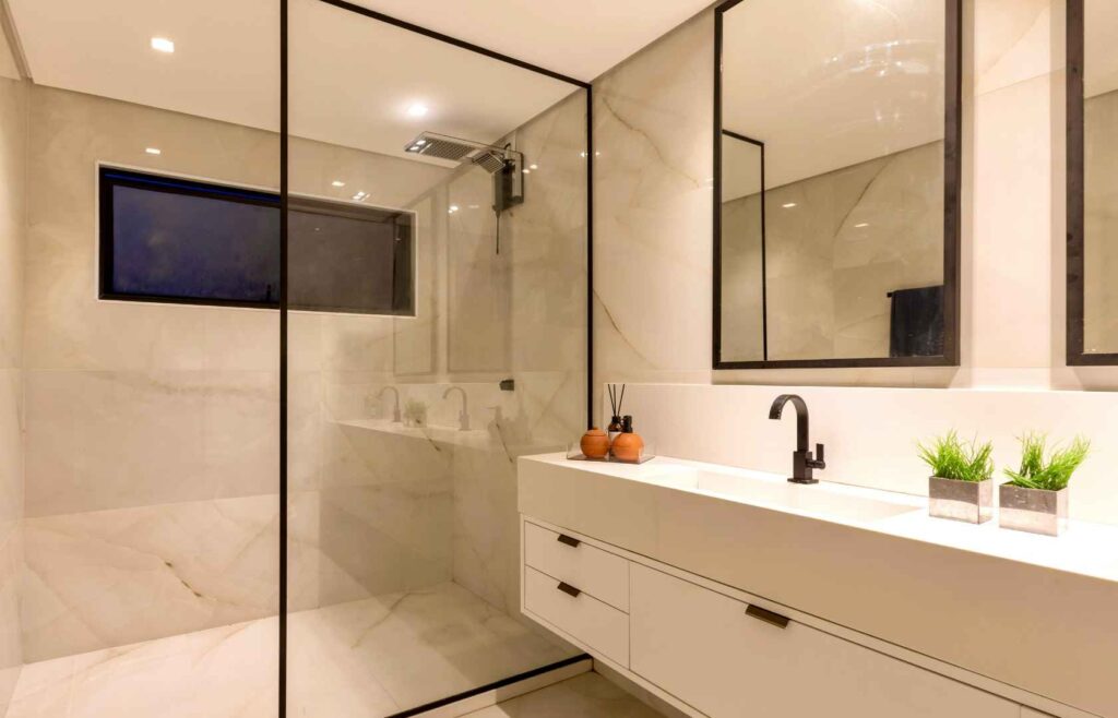 Shower maintenance by The Shower Repair Centre, showing a clean modern bathroom with glass shower screen, tiled shower area, vanity, mirror, and black fixtures.
