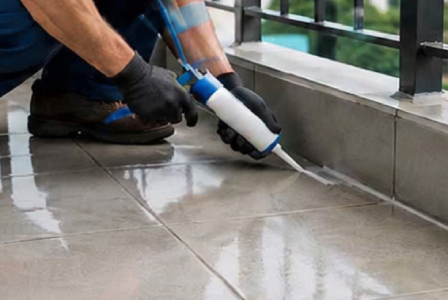 Technician applying sealant along a tiled balcony edge as part of balcony waterproofing of SRC.